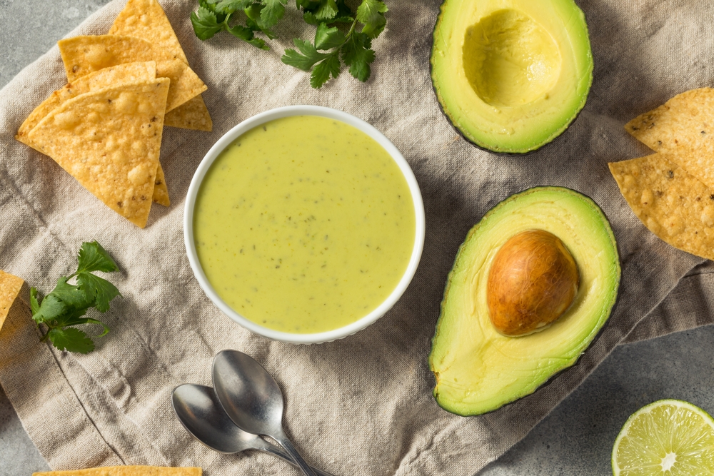 Flat lay of green avocado salsa surrounded by a whole avocado sliced in half and tortilla chips.