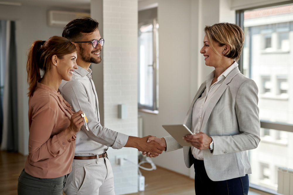 Female real estate agent shaking hands with a young couple.