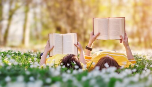 Mother and son laying in a grassy field reading books.