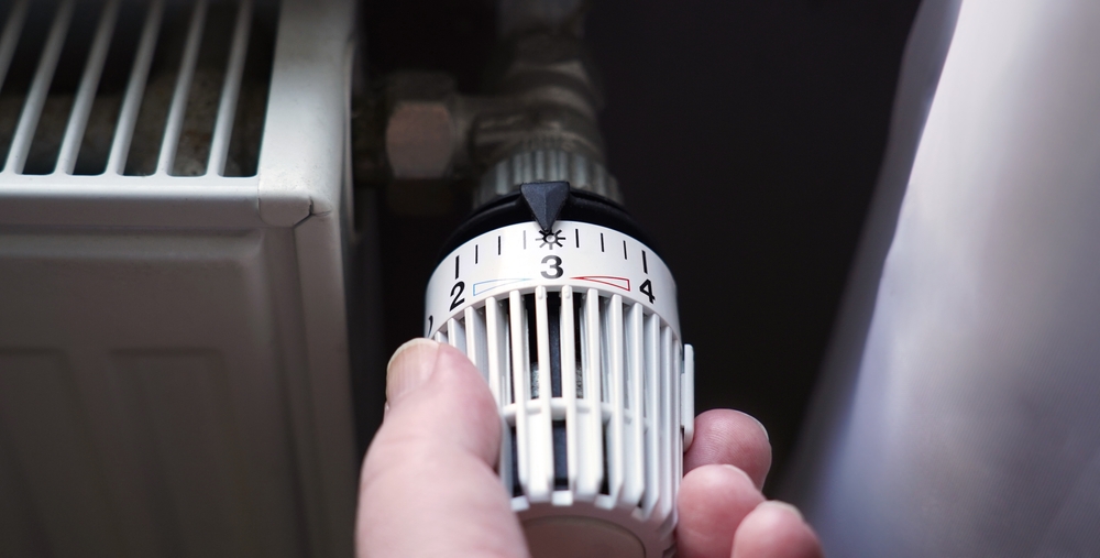 Person turning the thermostat dial on a radiator.