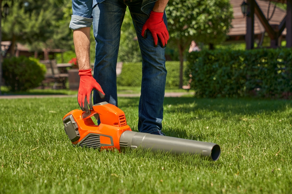 Person reaching down to pick up an orange leaf blower.