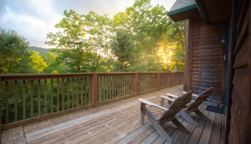 Two Muskoka chairs on a wooden porch surrounded by trees.