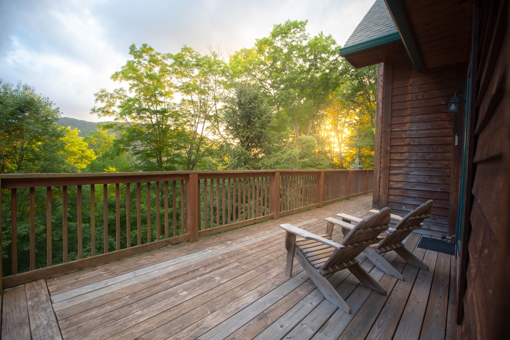 Two Muskoka chairs on a wooden porch surrounded by trees.