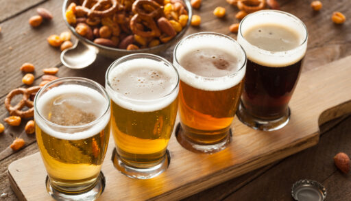 Flight of four different coloured beers with a bowl of pretzels in the background.