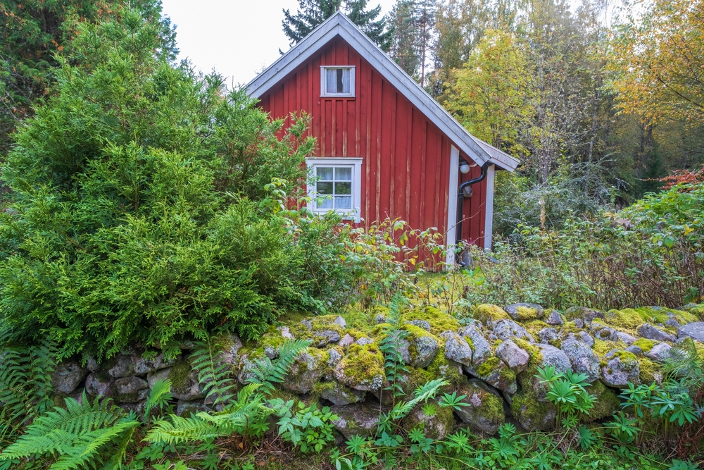 Red cottage surrounded by trees and a garden wall.