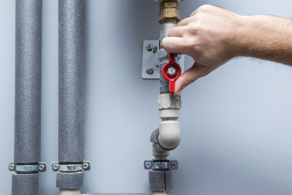Man turning a red water valve on a pipe.