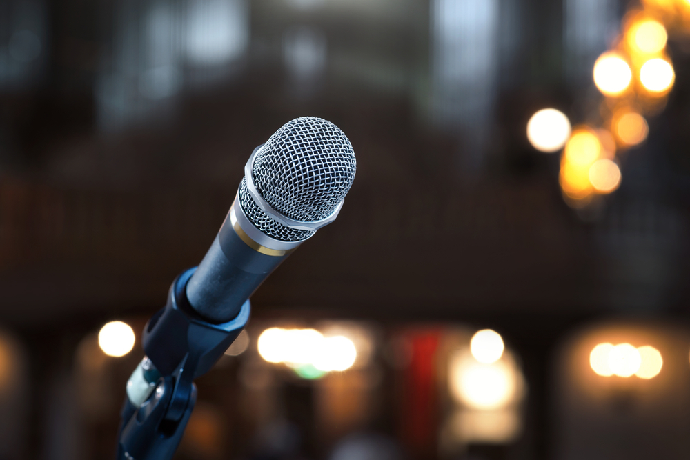 Silver microphone on a stand with a blurred crowd in the background.