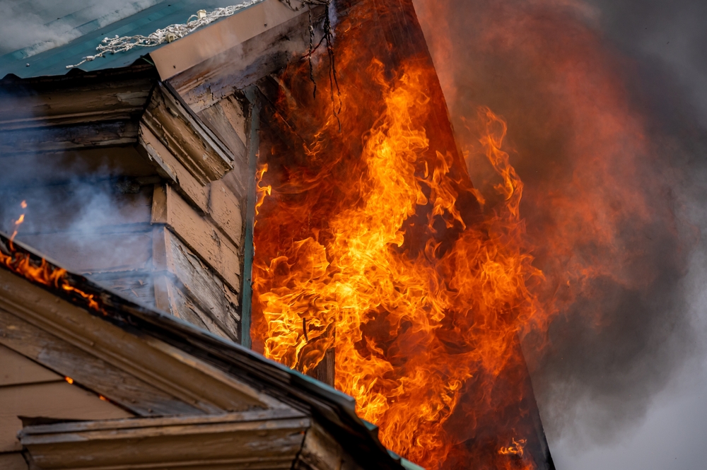 Wooden house with flames coming out of a window.