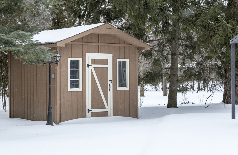 Brown shed covered in snow in a forest.