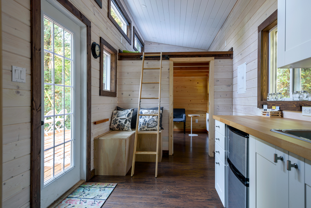 Interior of a tiny home with wood panelling, a small kitchen and a loft.