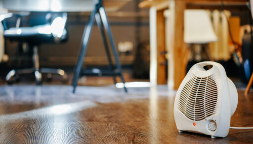 Small, white space heater in a room with tables and chairs.