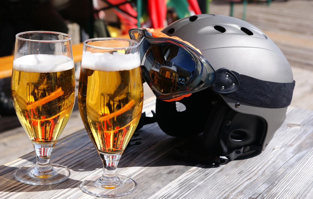 Two glasses of beer in front of a ski helmet on a table.