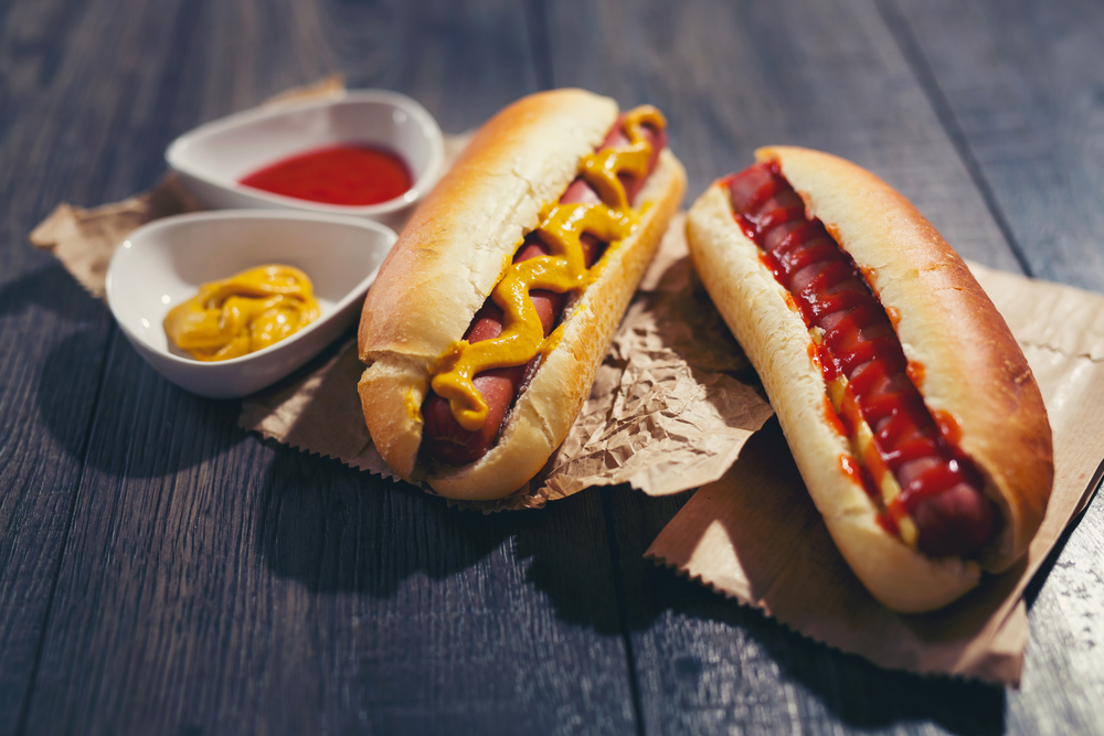 Two hot dogs covered in ketchup and mustard.