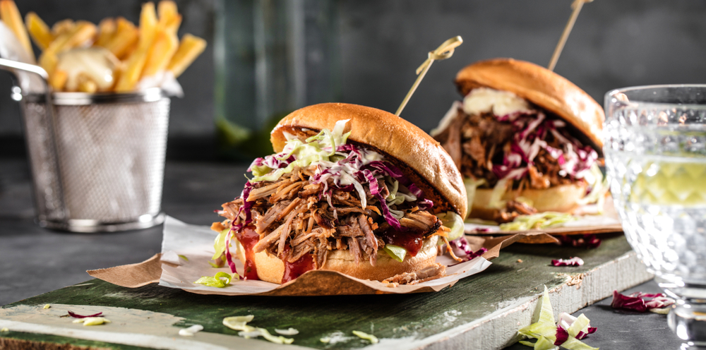 Two pulled pork sandwiches next to a basket of french fries.