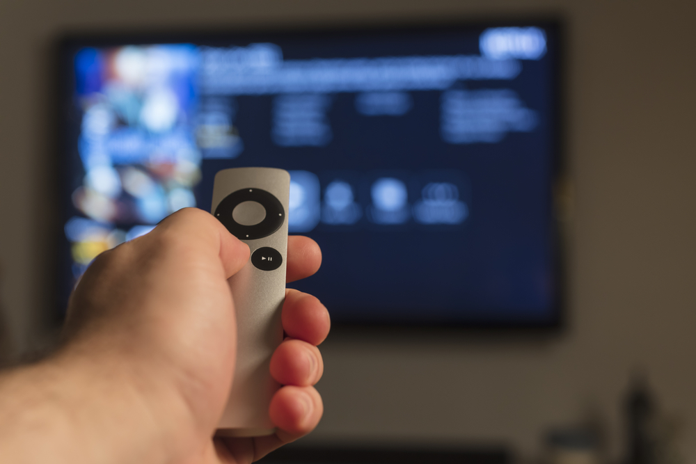 Person holding an Apple TV remote and pointing it at a television.