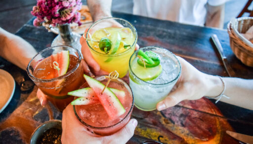 Four people sitting at a table holding cocktails and toasting.