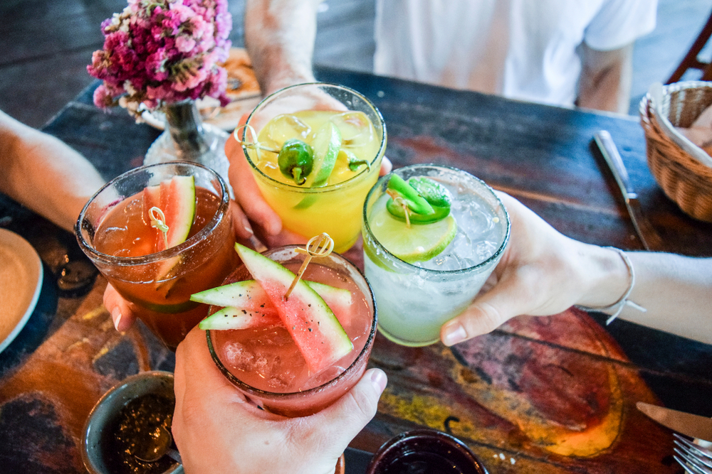 Four people sitting at a table holding cocktails and toasting.
