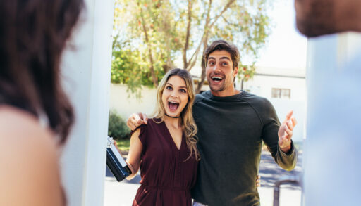 Excited couple greeting friends at a door.