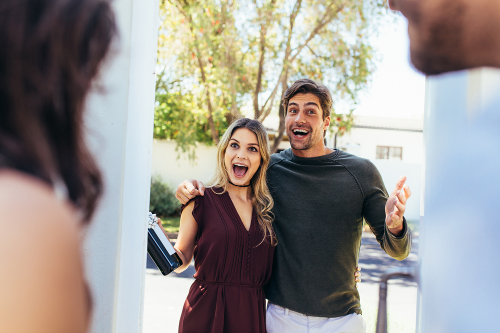 Excited couple greeting friends at a door.