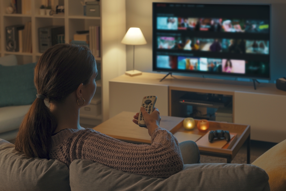 Young woman sitting on a couch and using a remote to select a movie.