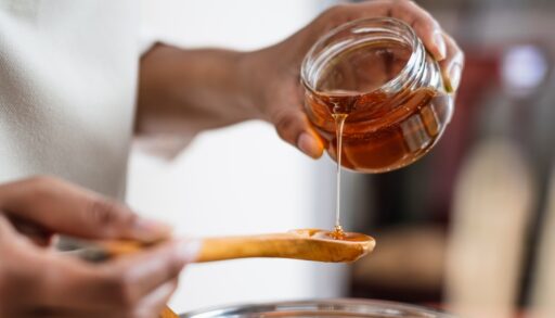 Close-up of a woman pouring honey from a jar onto a wooden spoon.