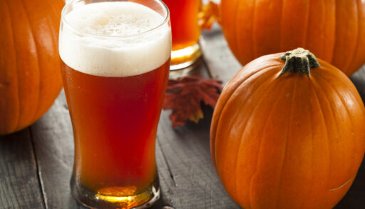 Frothy orange-coloured pumpkin beer on a table in front of a small pumpkin.