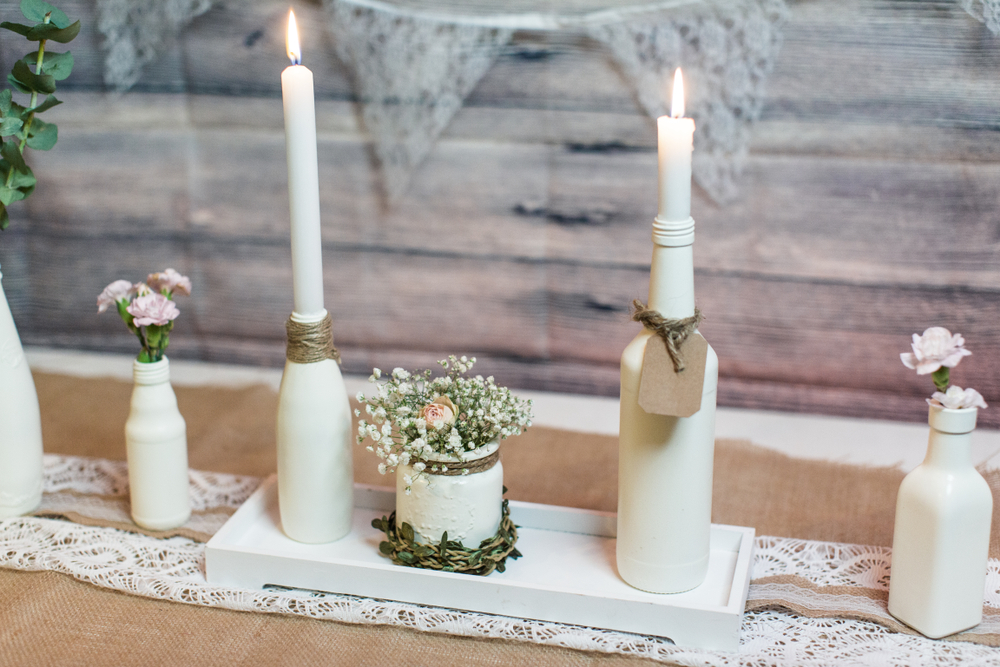 Wine bottles painted white and repurposed as candlesticks for a wedding arrangement.
