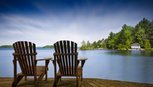 Muskoka chairs on a dock overlooking a lake.