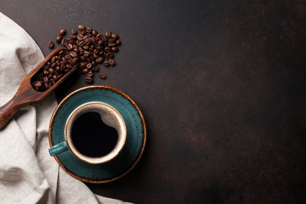 Overhead view of a teal coffee cup with a wooden scoop of coffee beans next to it.