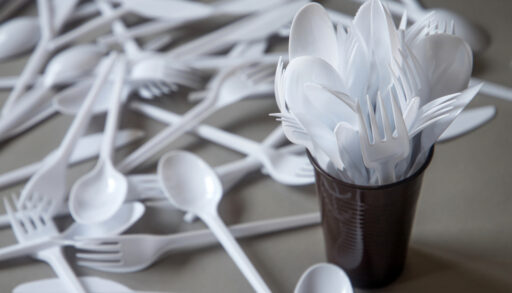 Close-up of a plastic cup filled with white, disposable plastic cutlery.