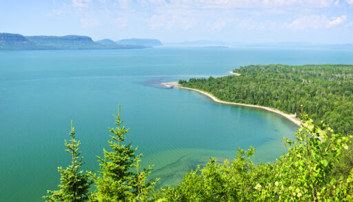 Aerial view of a turquoise-coloured Lake Superior, surrounded by a green forest.