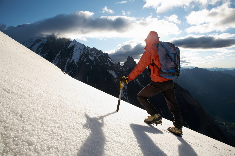 Mountain climber wearing boots with spikes hiking the side of a mountain in winter.