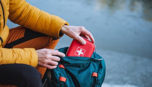 Close-up of a person putting a red first aid kit into a green backpack.