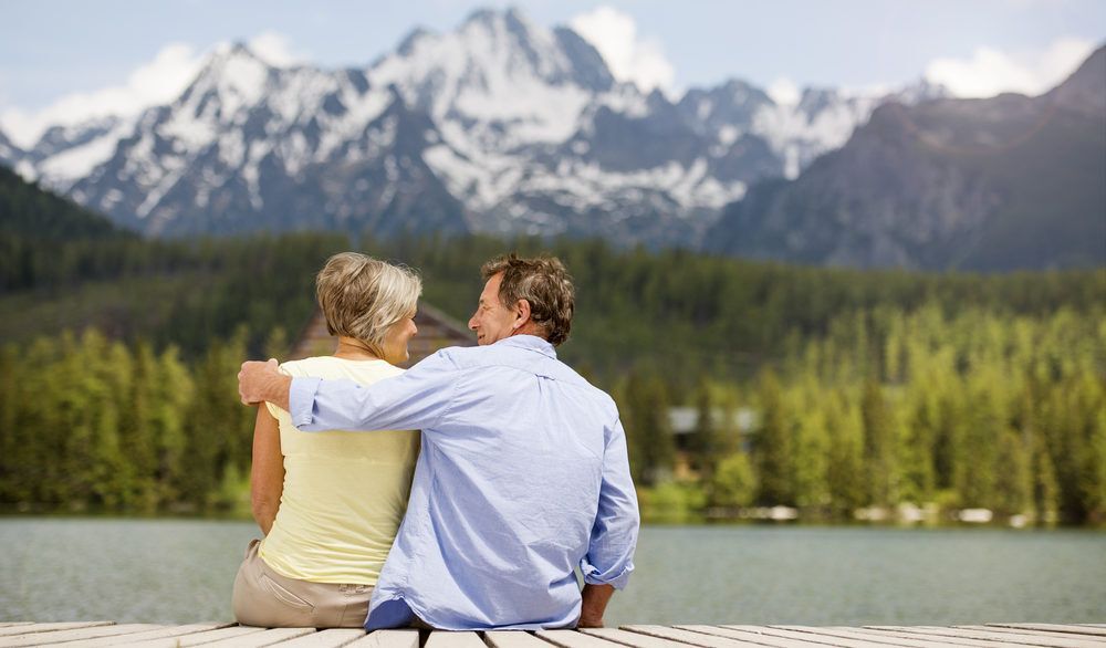 Retired couple sitting on a dock with mountains in the background.
