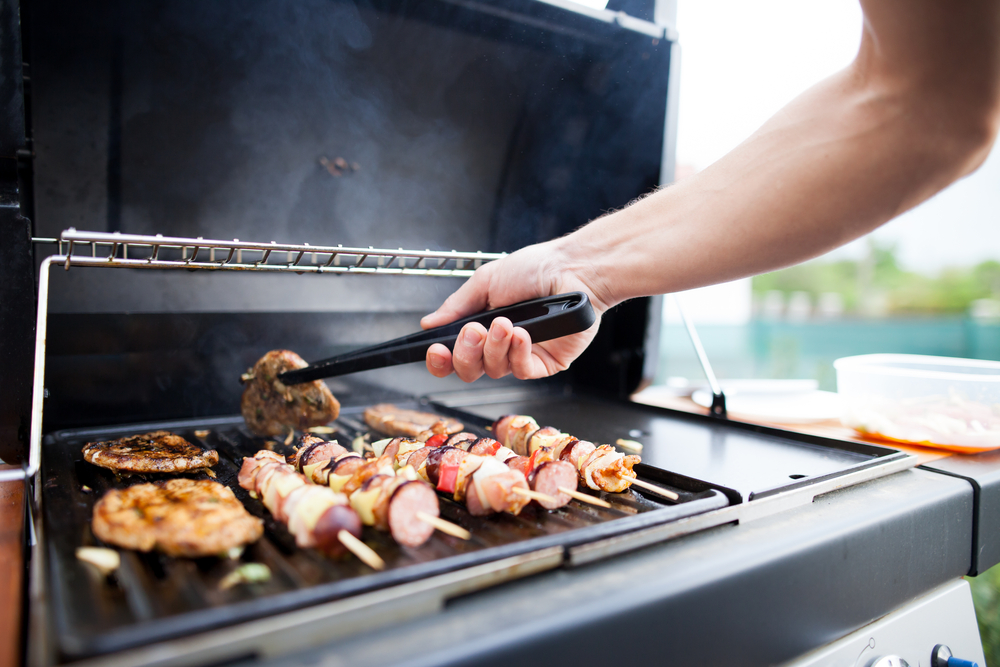 Close-up of a man's hand using tongs to flip steak on a grill.