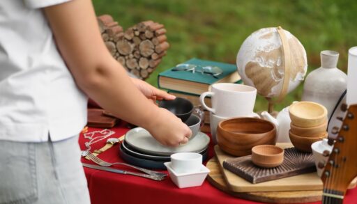 Close-up of a woman picking up dishes off a table at a yard sale.