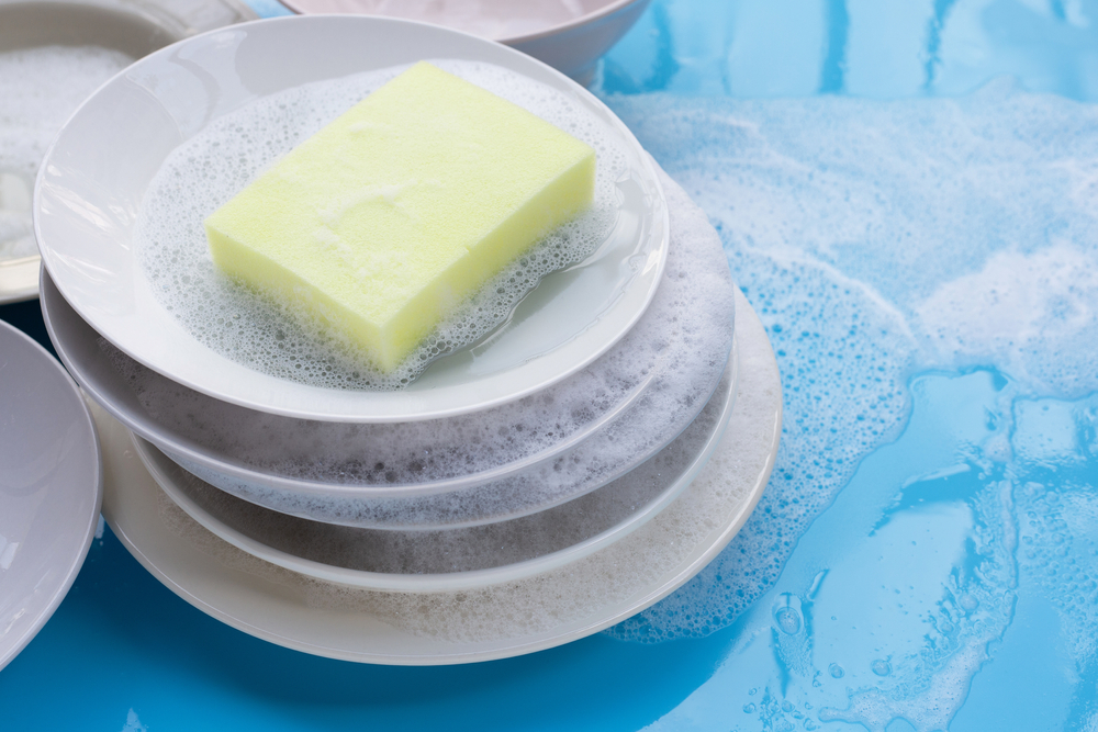 Stack of soap-covered dishes with a yellow sponge sitting on top.