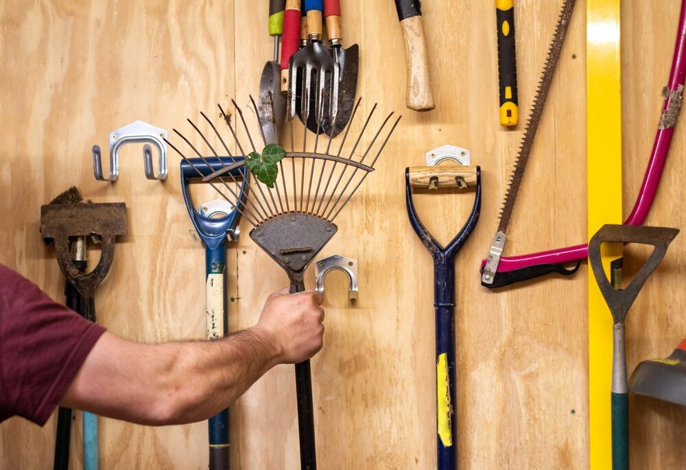 Close-up of a man taking a garden rake off a tool rack.