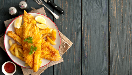 Overhead view of a plate of fish and chips next to a fork and knife.