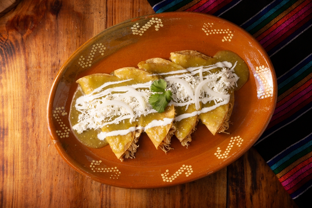 Overhead view of chicken enchiladas with a white sauce on a red plate.