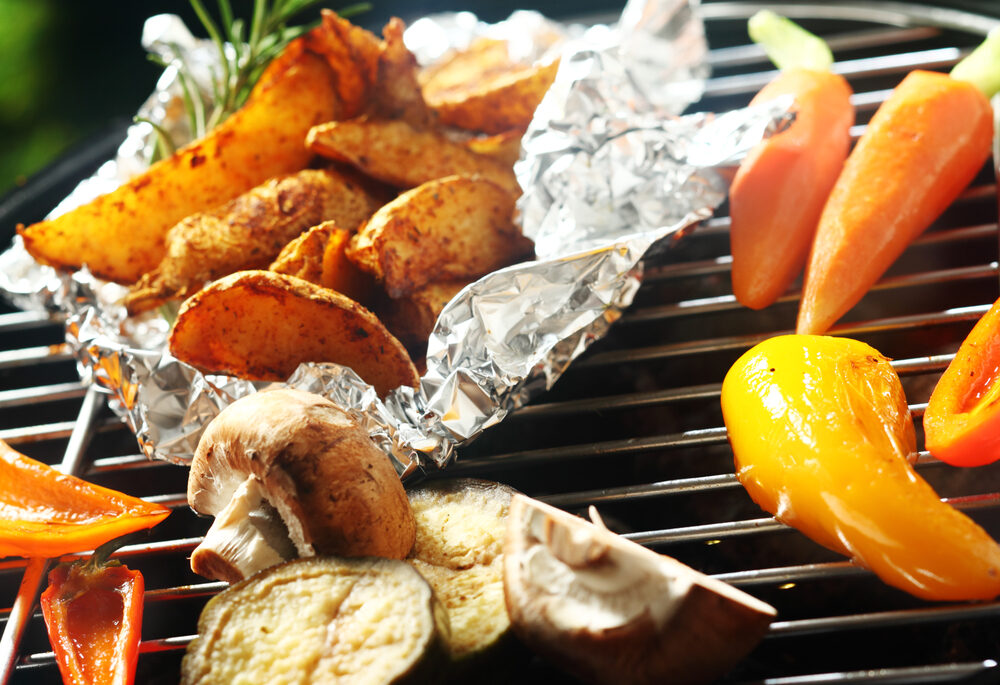 Close-up of potatoes being grilled in foil along with other vegetables.