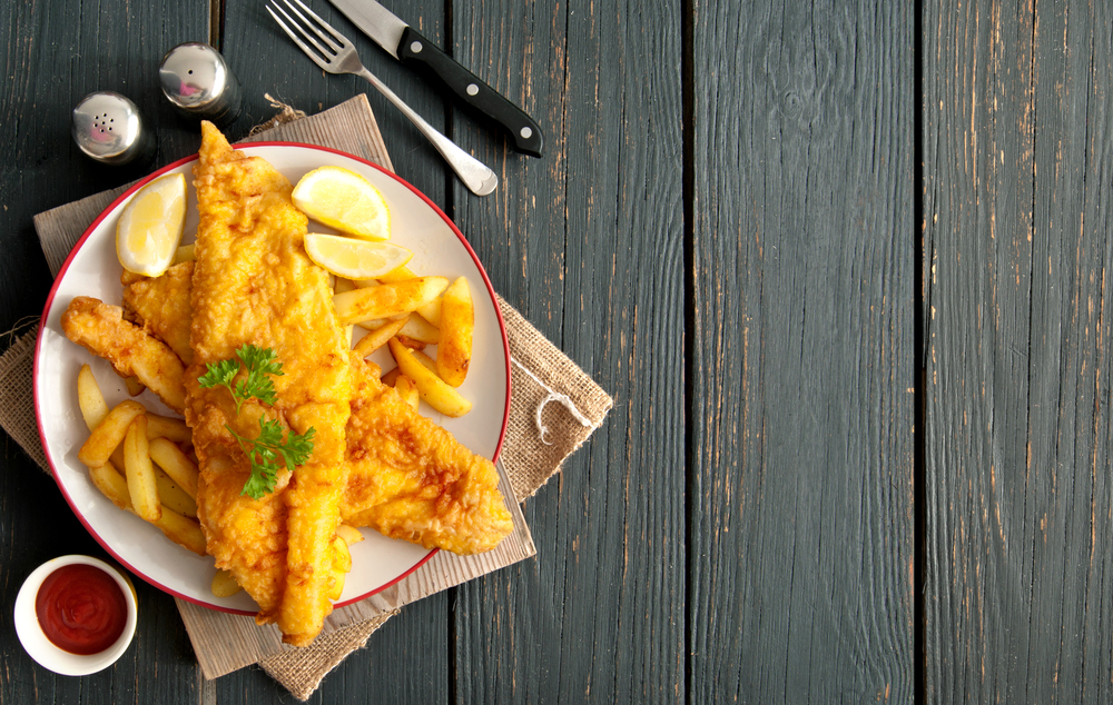 Overhead view of two pieces of fried fish on a plate next to a fork and knife.
