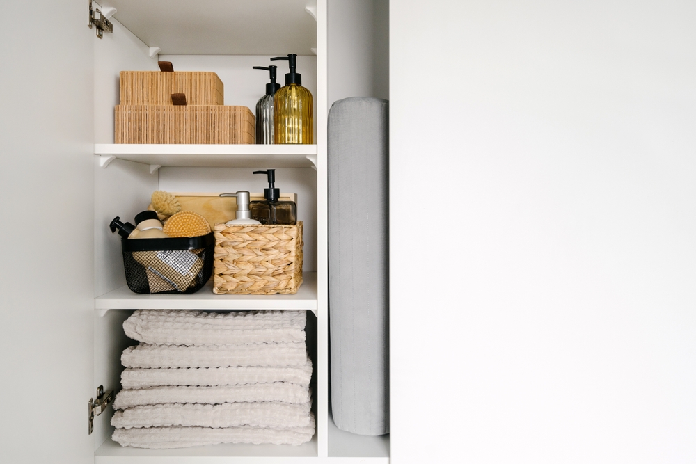 A bathroom closet with folded grey towels and wicker baskets for storage.