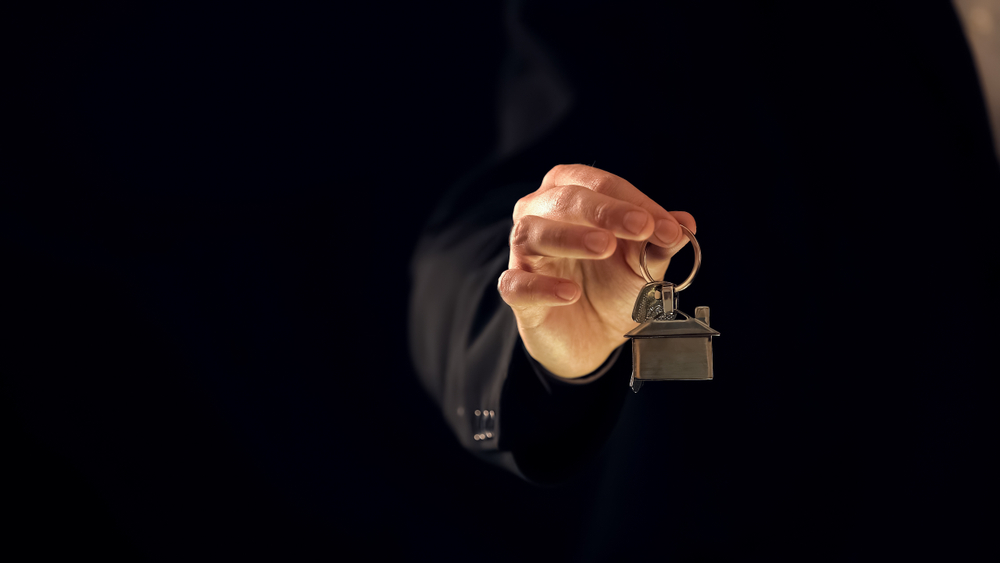 Close-up of a man's hand holding a keychain with a house on it.