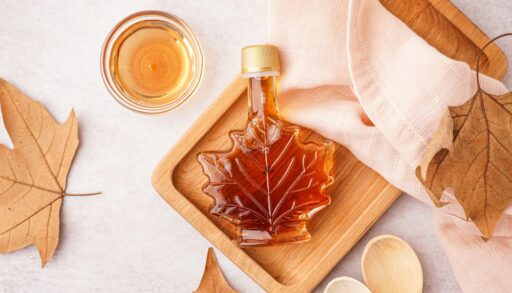 Maple leaf shaped jar of maple syrup on a brown tray.