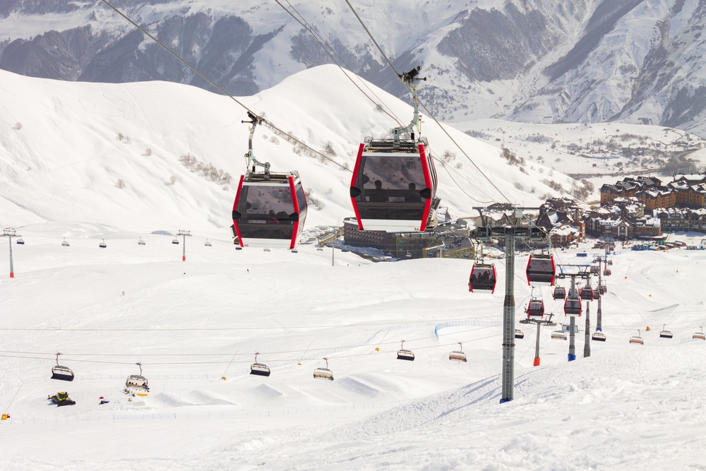 Red ski gondola going up a snow covered ski hill.