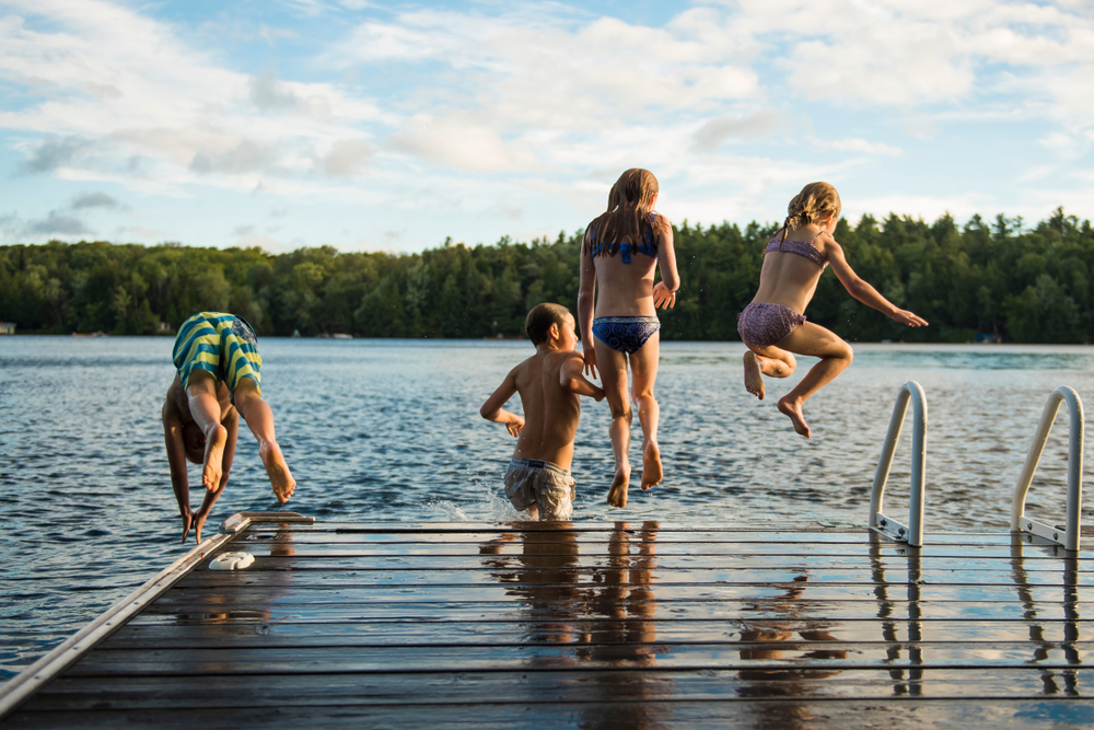 Four kids jumping off a dock into a lake.
