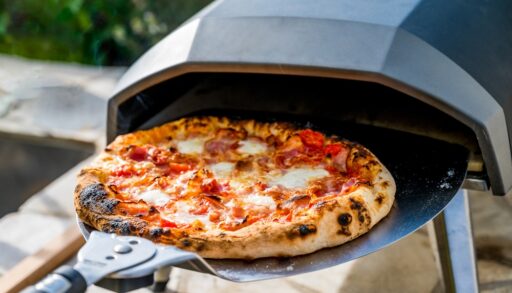 Pizza being taken out of an outdoor pizza oven.