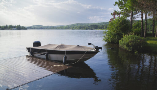 Covered motor boat on a lake tied to a dock.