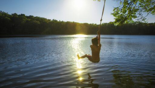 Boy swinging into a lake on a rope swing at sunset.
